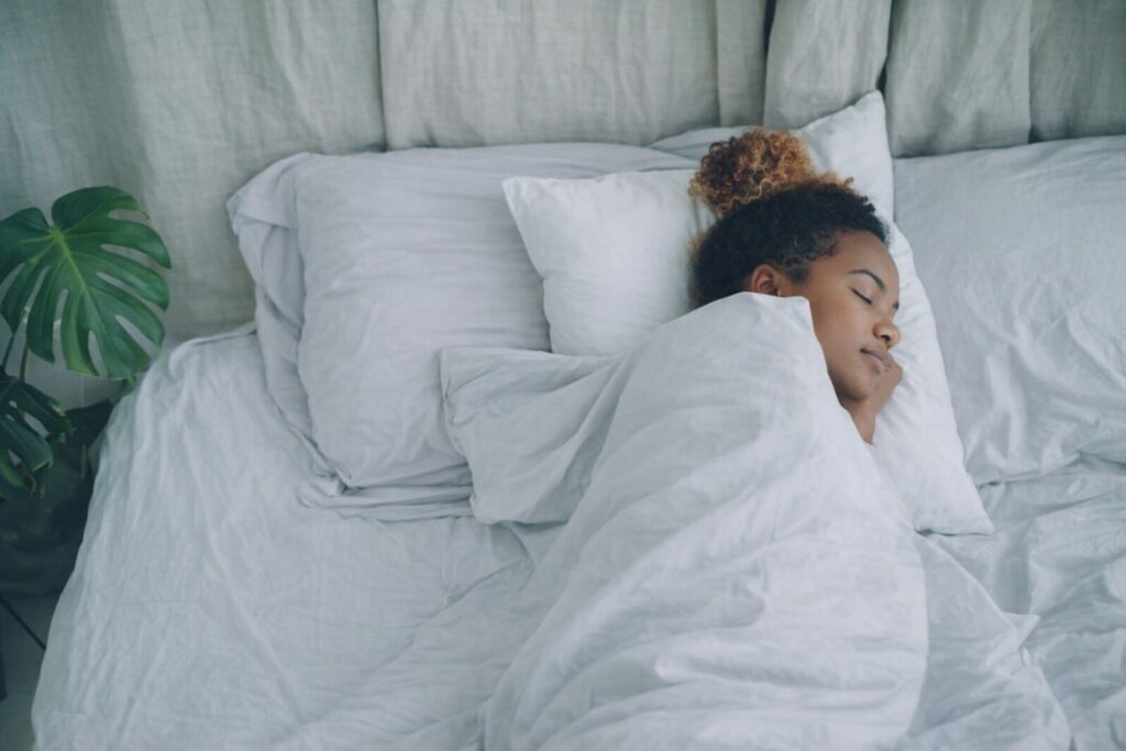 En kvinna som sover djupt och fridfullt i en säng med vita lakan.