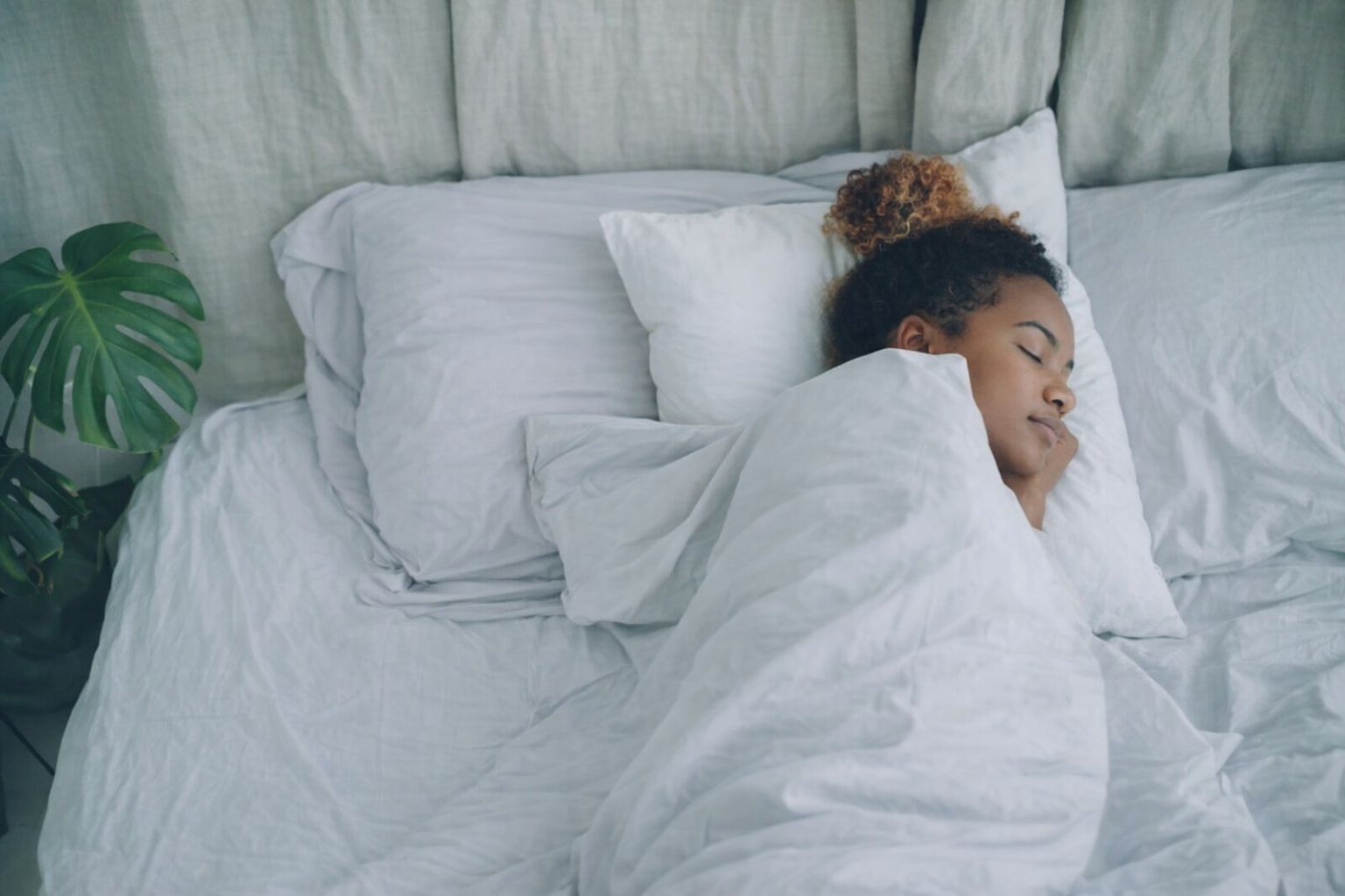 En kvinna som sover djupt och fridfullt i en säng med vita lakan.